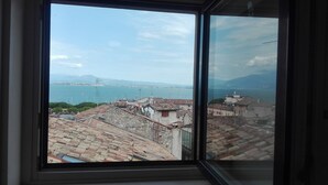 A view through a window of a coastal cityscape with buildings, a bridge, and mountains in the distance. - Appartment with unique view on the Garda Lake (Desenzano del Garda)