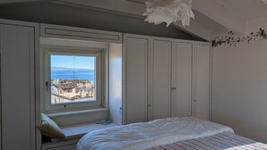 A bedroom with a large window offering a view of a coastal town, white furniture, and a ceiling light fixture. - Appartment with unique view on the Garda Lake (Desenzano del Garda)