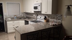 A kitchen with white cabinets, a granite countertop, a microwave, a stove, and a coffee maker.