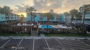 A pool area with lounge chairs and a wooden fence, surrounded by blue buildings with balconies.