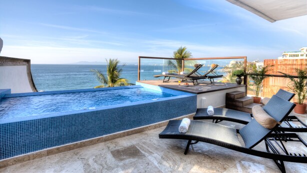 A rooftop infinity pool with lounge chairs, a small table, and potted plants.