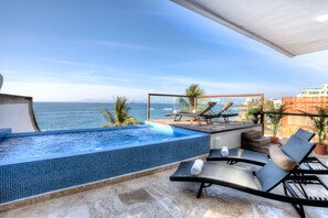 Ein Dachpool mit Infinity-Kante, Liegestühlen, einem kleinen Tisch und Topfpflanzen.