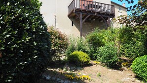 Un jardin agrémenté de diverses plantes et fleurs, une terrasse en bois et un bâtiment doté d’un balcon.