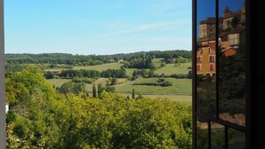 Une vue d’un paysage rural avec des collines douces, des arbres dispersés et quelques bâtiments.