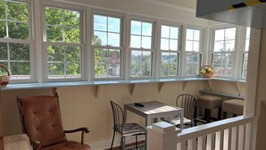 A sunlit room with a large window, a wooden chair, a small table, and a radiator.