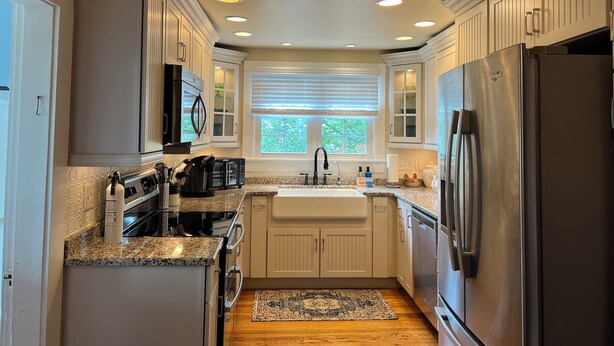 A modern kitchen with white cabinetry, granite countertops, a stainless steel refrigerator, and a window with blinds.