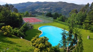 Una piscina rodeada de exuberante vegetación y una cancha de tenis, con montañas al fondo.