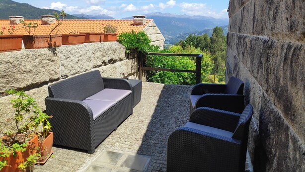 Terraza en la azotea con mobiliario de mimbre, plantas en macetas y un muro de piedra.