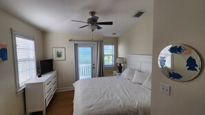 Un dormitorio con cama, ventilador de techo, cómoda, televisor y puerta que da a un balcón.