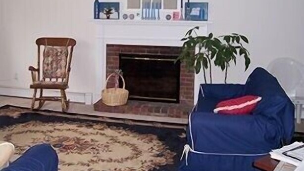 Una sala de estar con chimenea, un sofá azul, una silla de madera y una alfombra estampada.