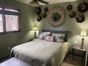 A bedroom with a bed, two bedside tables, a ceiling fan, a large mirror, and decorative pine cones on the wall. - Renovated Home on Acre. Sunset Cliff Experience. Pets. Two Full Bathrooms. (Rapid City)