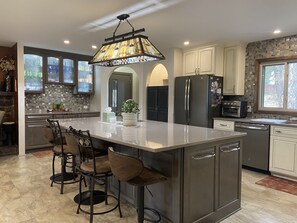 A modern kitchen with a large island, bar stools, a refrigerator, and a built-in oven. - Renovated Home on Acre. Sunset Cliff Experience. Pets. Two Full Bathrooms. (Rapid City)