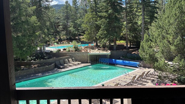 Et poolområde med flere pools, liggestole og skov i baggrunden.