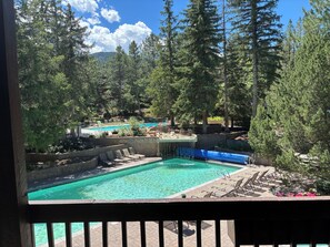 A pool area with multiple pools, lounge chairs, and a forested backdrop.