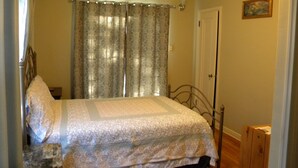 Une chambre à coucher avec un lit, des rideaux, une porte et un tableau au mur.
