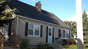 Une maison à deux étages avec un porche à l’avant, une cheminée et une antenne parabolique.