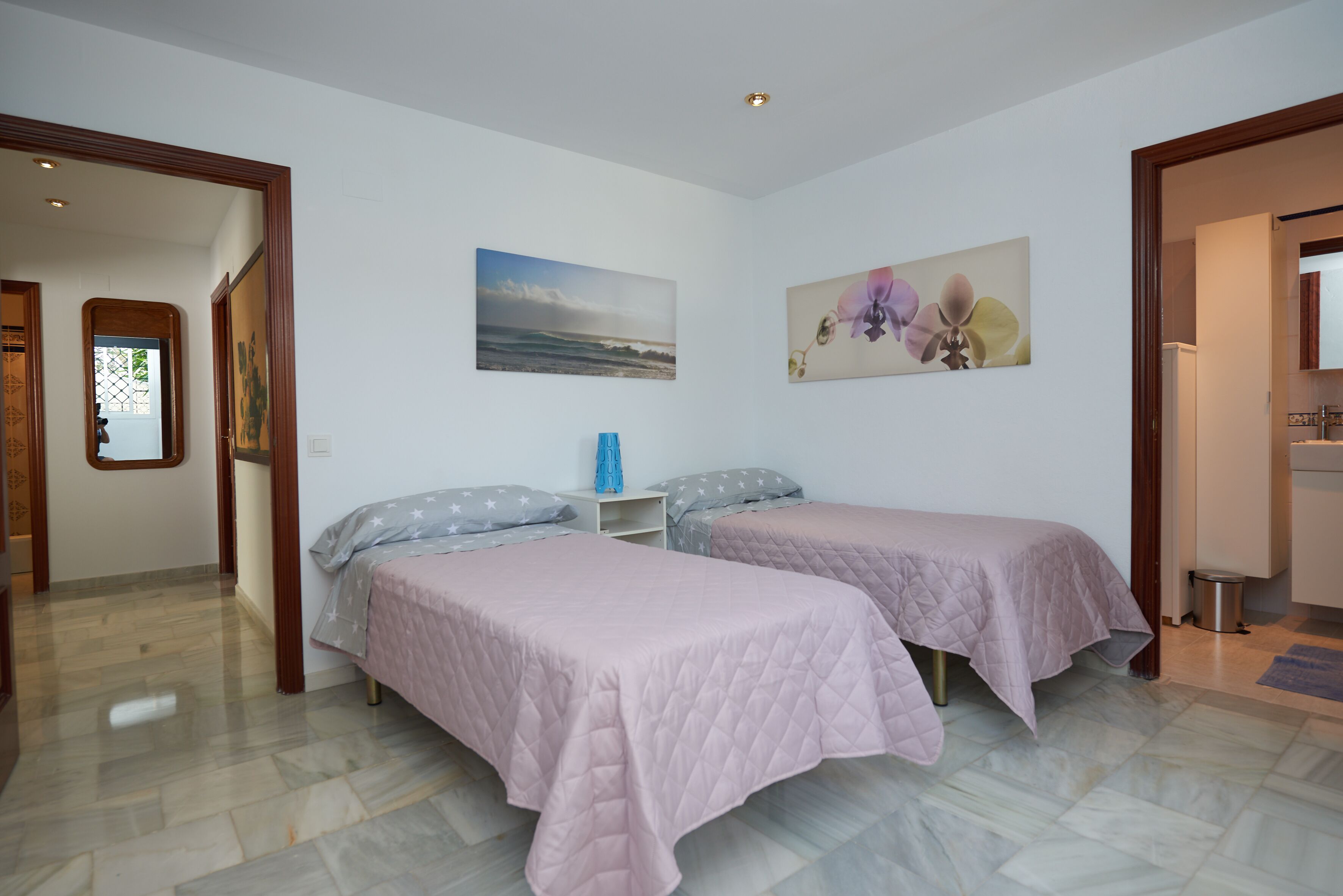 A bedroom with two beds, a nightstand, and a painting of flowers.