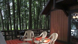 An outdoor seating area with a wooden table and four white plastic chairs, surrounded by a wooden deck and a forest backdrop. - Spectacular Location  Reasonably Priced (Belgrade)