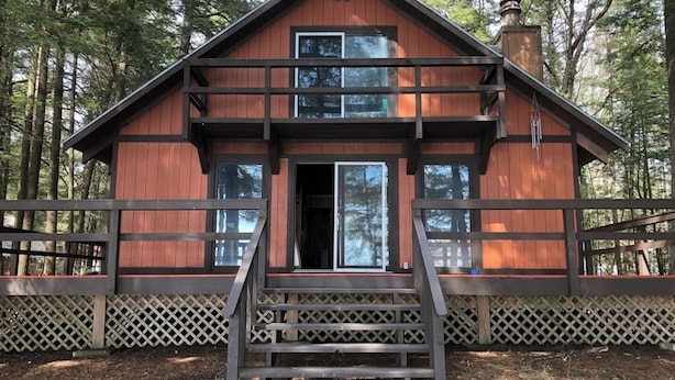 A two-story cabin with a wooden exterior, a front porch with steps, and a lattice fence surrounding the property. - Spectacular Location  Reasonably Priced (Belgrade)