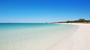 A beach with clear turquoise water, white sand, and sparse vegetation along the shore.