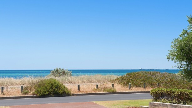 A coastal road with a clear view of the sea and a bridge in the distance.
