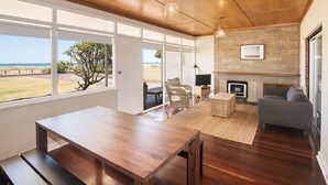 A modern living room with a wooden table, a grey sofa, and a fireplace. - BOWERBIRD VIEW - Breathtaking Ocean Views (Busselton)