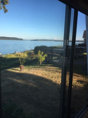 A view from a window overlooking a lake with a distant mountain, a grassy area with a potted plant, and a clear sky. - Seashore Rental with Beach Access and Panoramic Sound View (Manchester)
