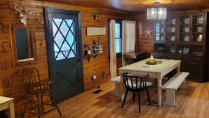 A rustic wooden interior with a dining table, chairs, a bench, a wooden door, and a cabinet with glass doors.