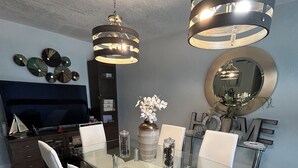 A modern dining area with a glass table, white chairs, and two pendant lights. A decorative vase with flowers is on the table, and a large mirror hangs on the wall. - Fantastic Lakefront Home With Private Yard and Pool (Fort Lauderdale)