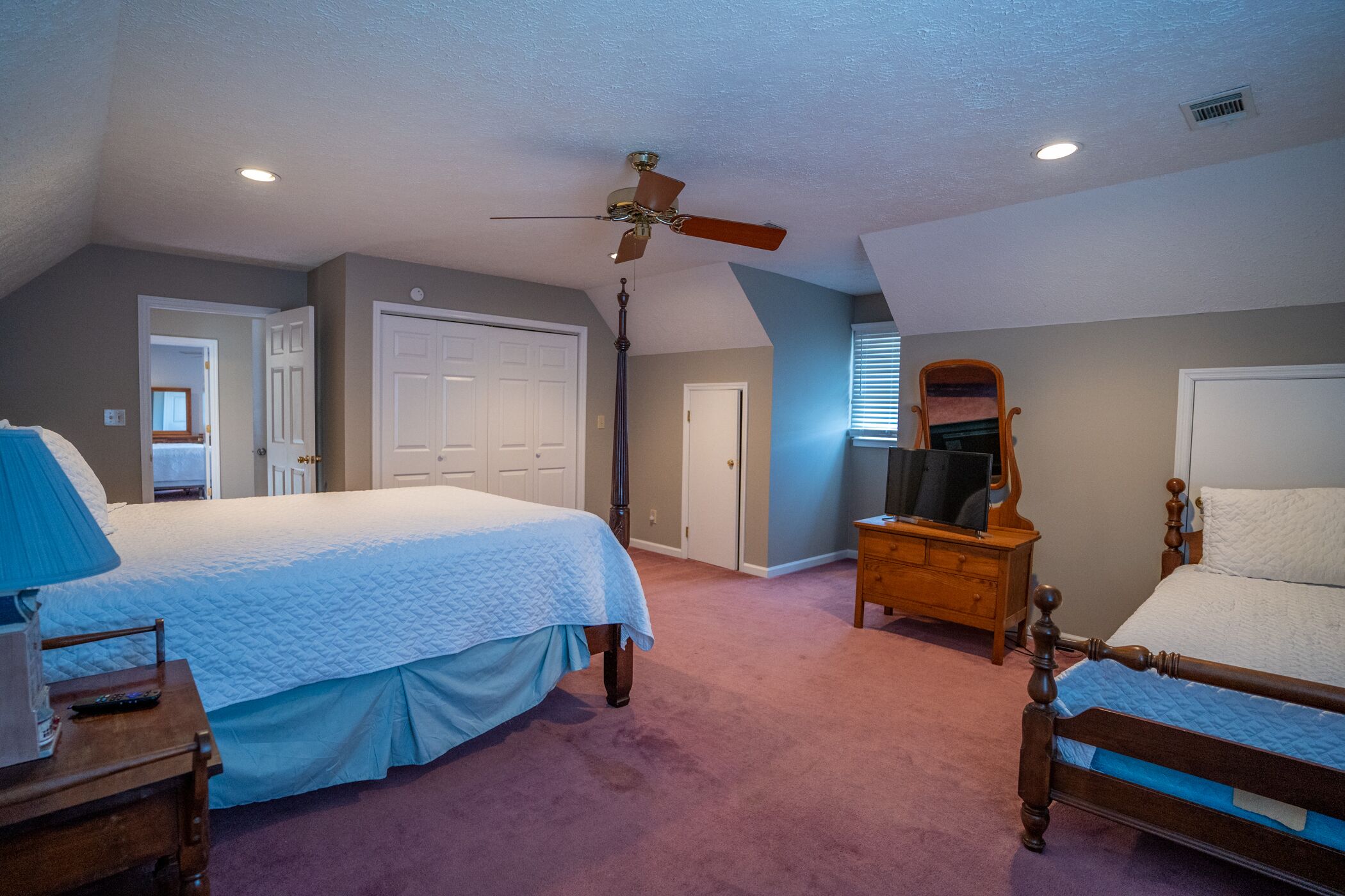 A bedroom with two beds, a ceiling fan, a dresser, and a television.