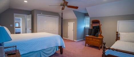 A bedroom with two beds, a ceiling fan, a dresser, and a television.