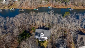 An aerial view of a house surrounded by trees and a lake with docked boats.