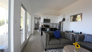 A modern living room with a grey sofa, a coffee table with a vase of sunflowers, and a view into the kitchen area. - Malibu Getaway-Relaxation Destination-Ocean view-Beaches, Hiking, Shops, Dining (Malibu)