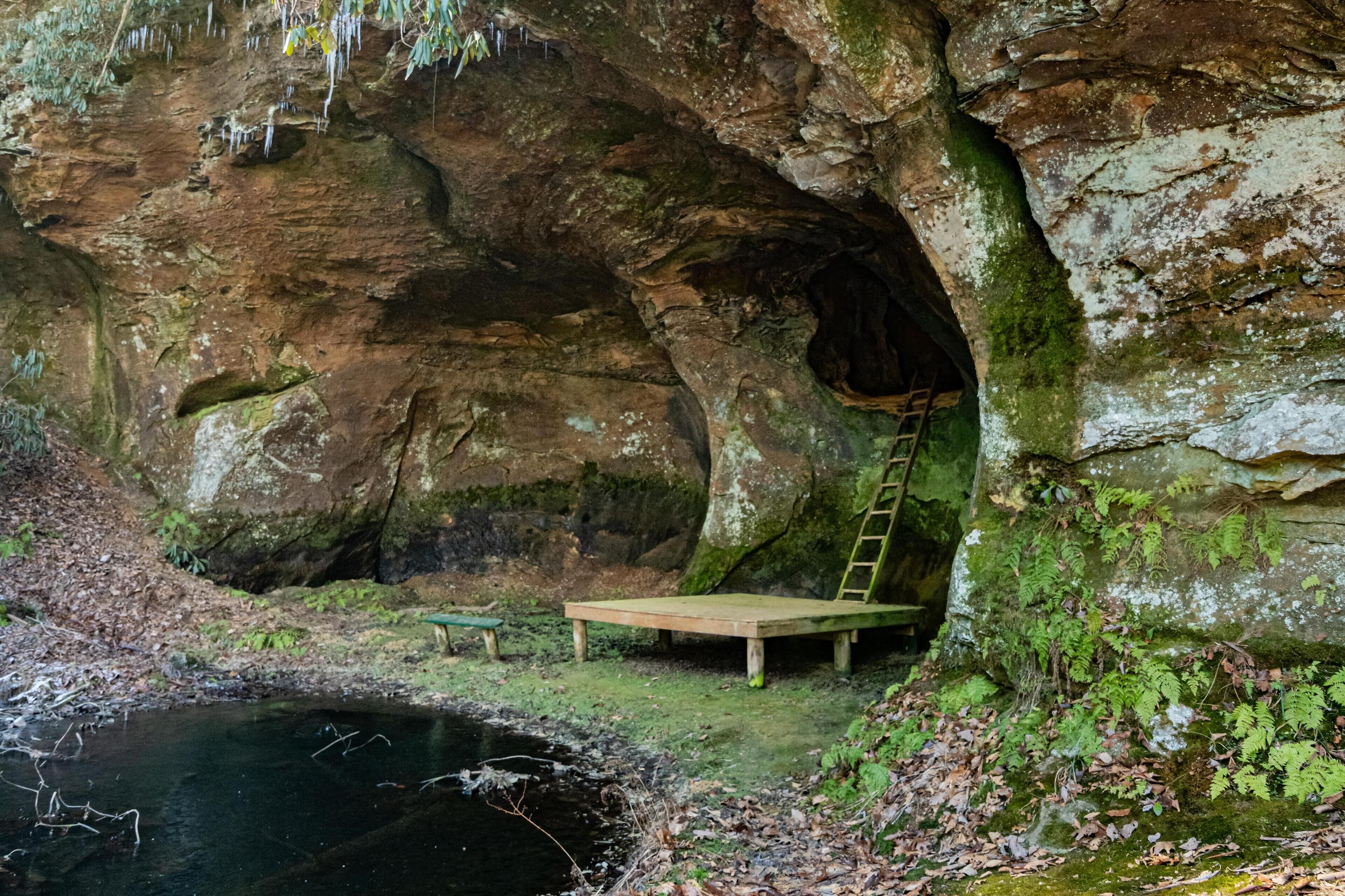 A cave entrance with a wooden bench and a ladder.