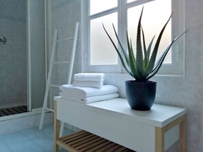 Ein Badezimmer mit weißem Waschtisch, einem Topf mit Aloe Vera und ordentlich gestapelten weißen Handtüchern.