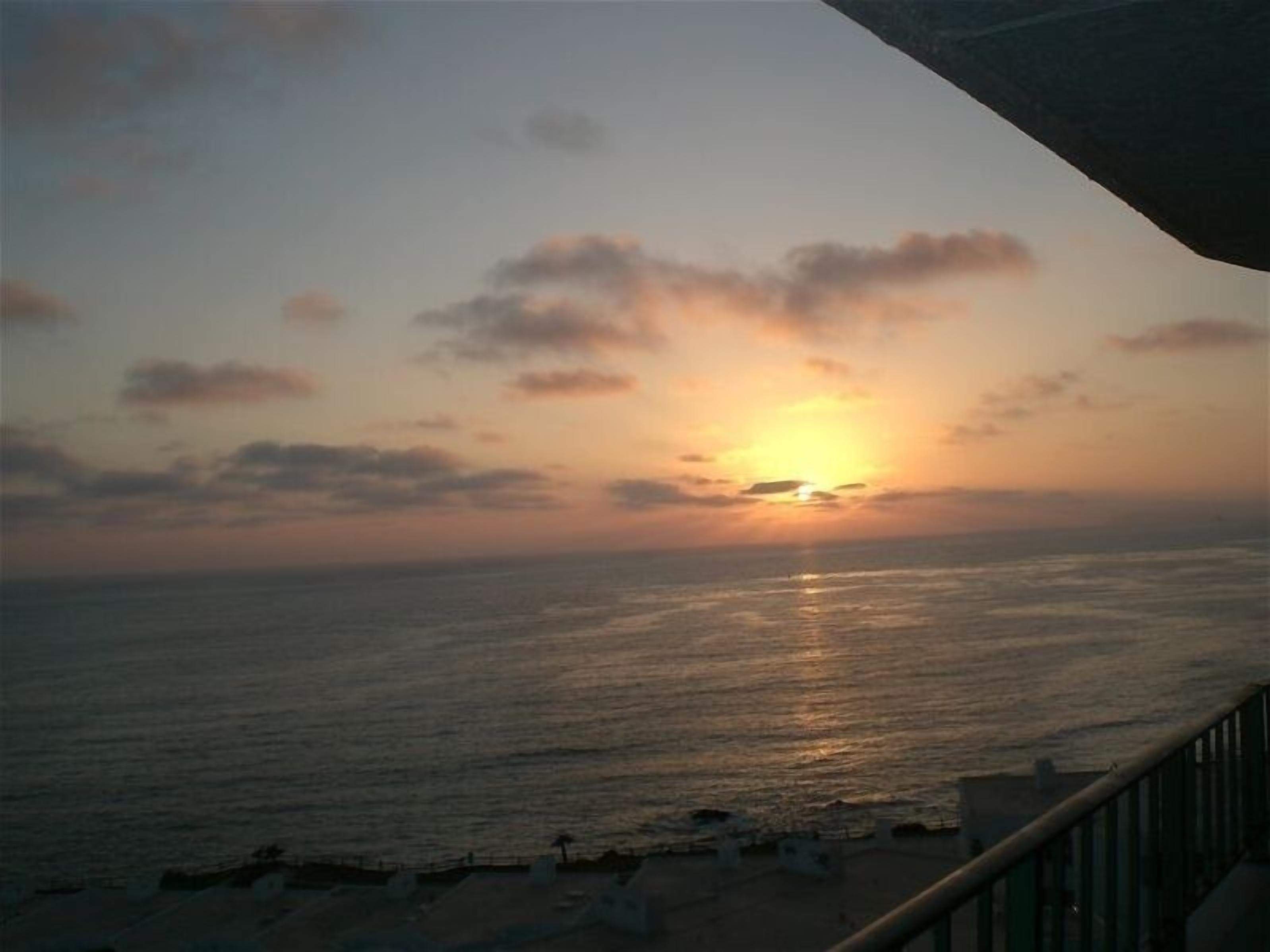 A sunset over the ocean with a view of the beach and a railing.