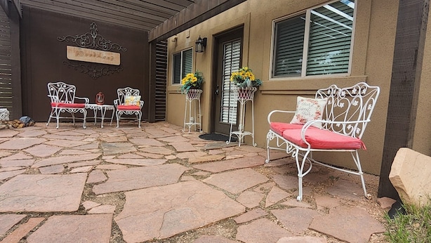 A patio with stone flooring, white metal chairs, and a bench. There are flower pots with yellow flowers and a sign that reads "Woodland." - Cozy guest apartment conveniently located to all Woodland Park attractions (Woodland Park)