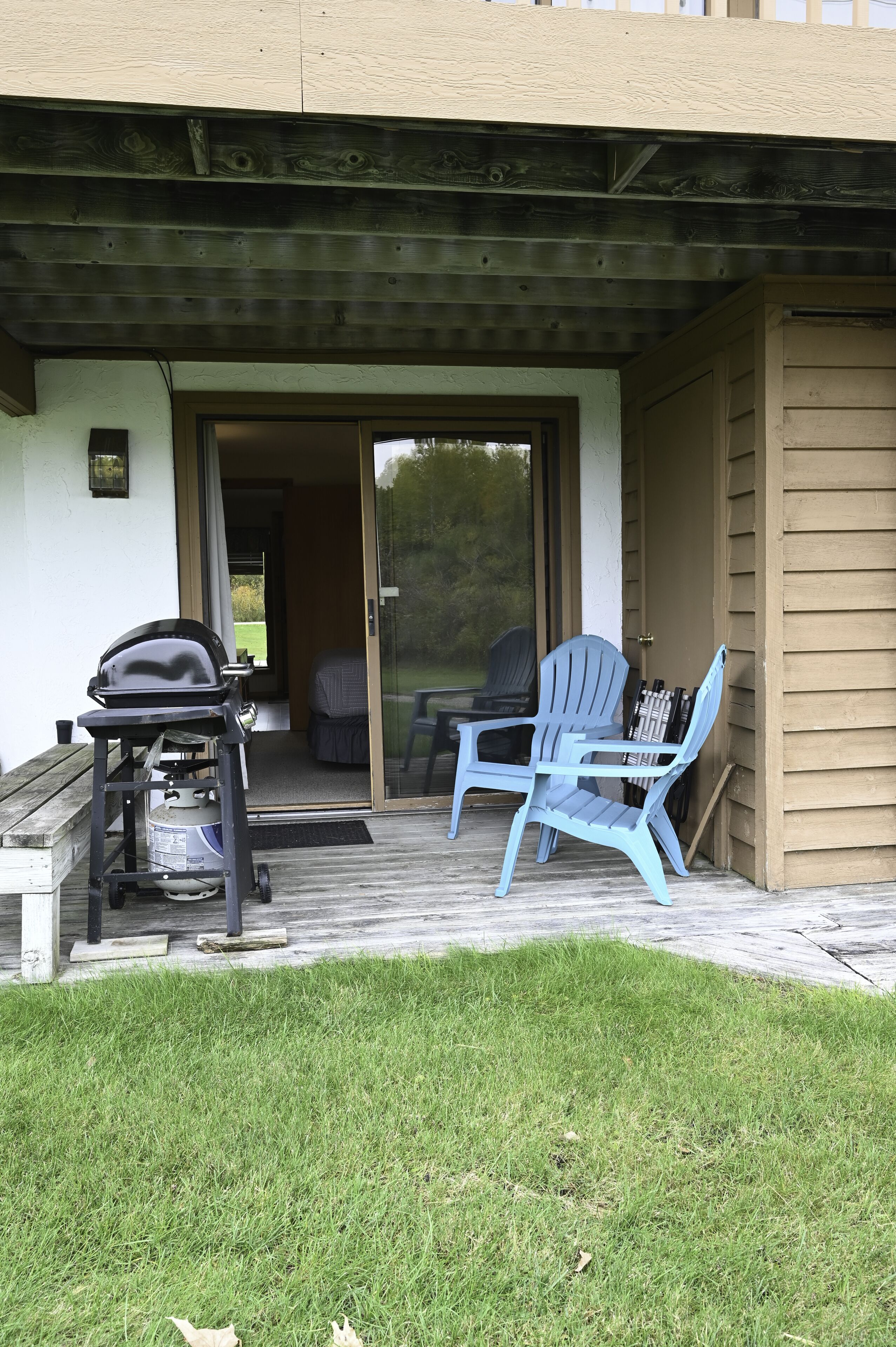 A covered patio with a grill, two Adirondack chairs, and a door leading to a room.