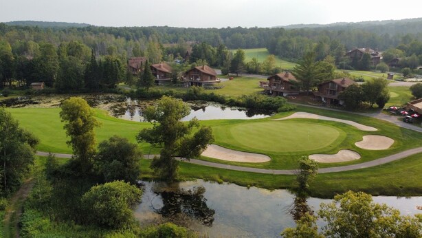 Un campo de golf con búnkeres, un estanque y casas al fondo.