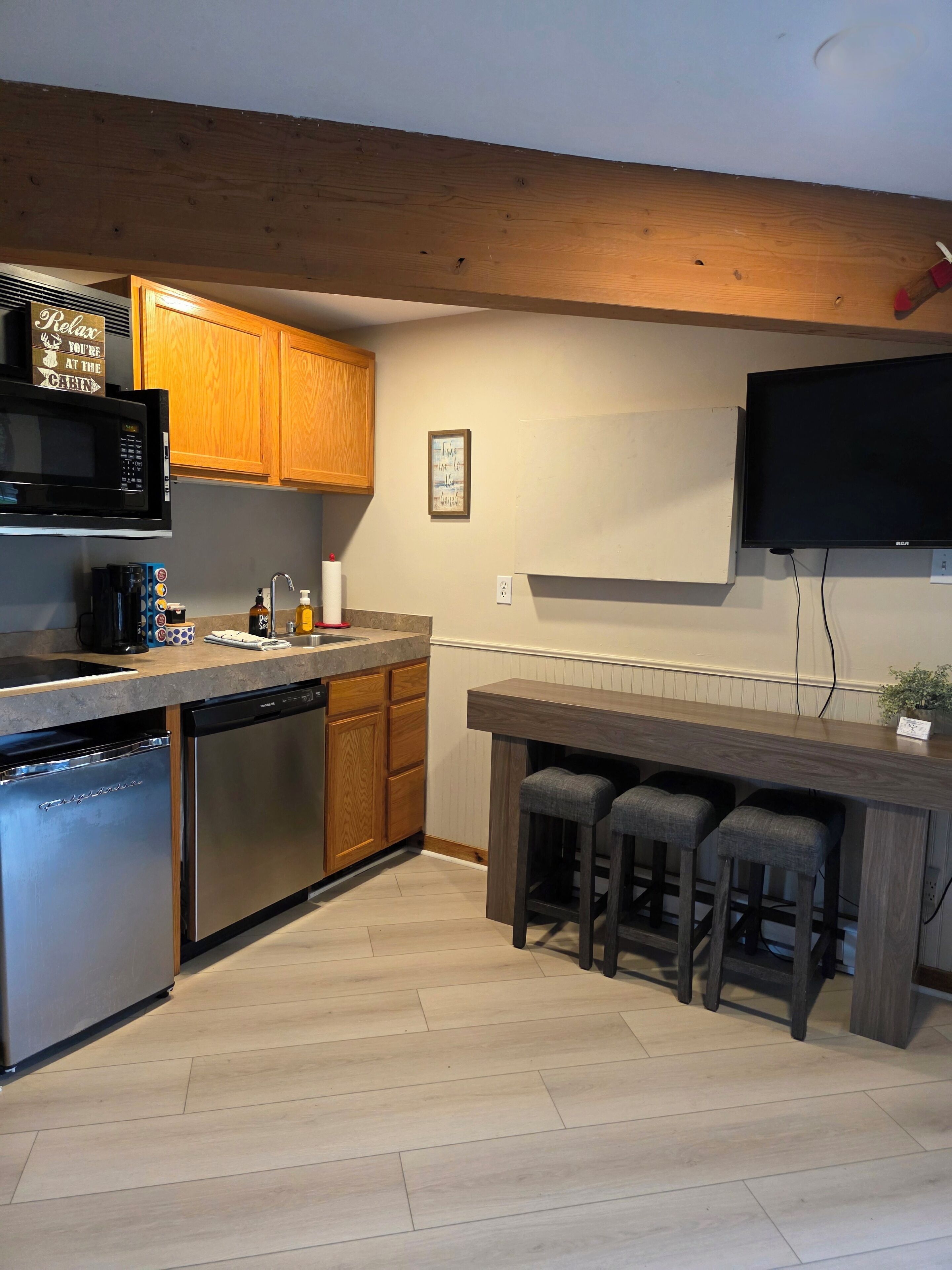 Una cocina moderna con armarios de madera, electrodomésticos de acero inoxidable, una zona de bar con taburetes y un televisor de pantalla plana montado en la pared.