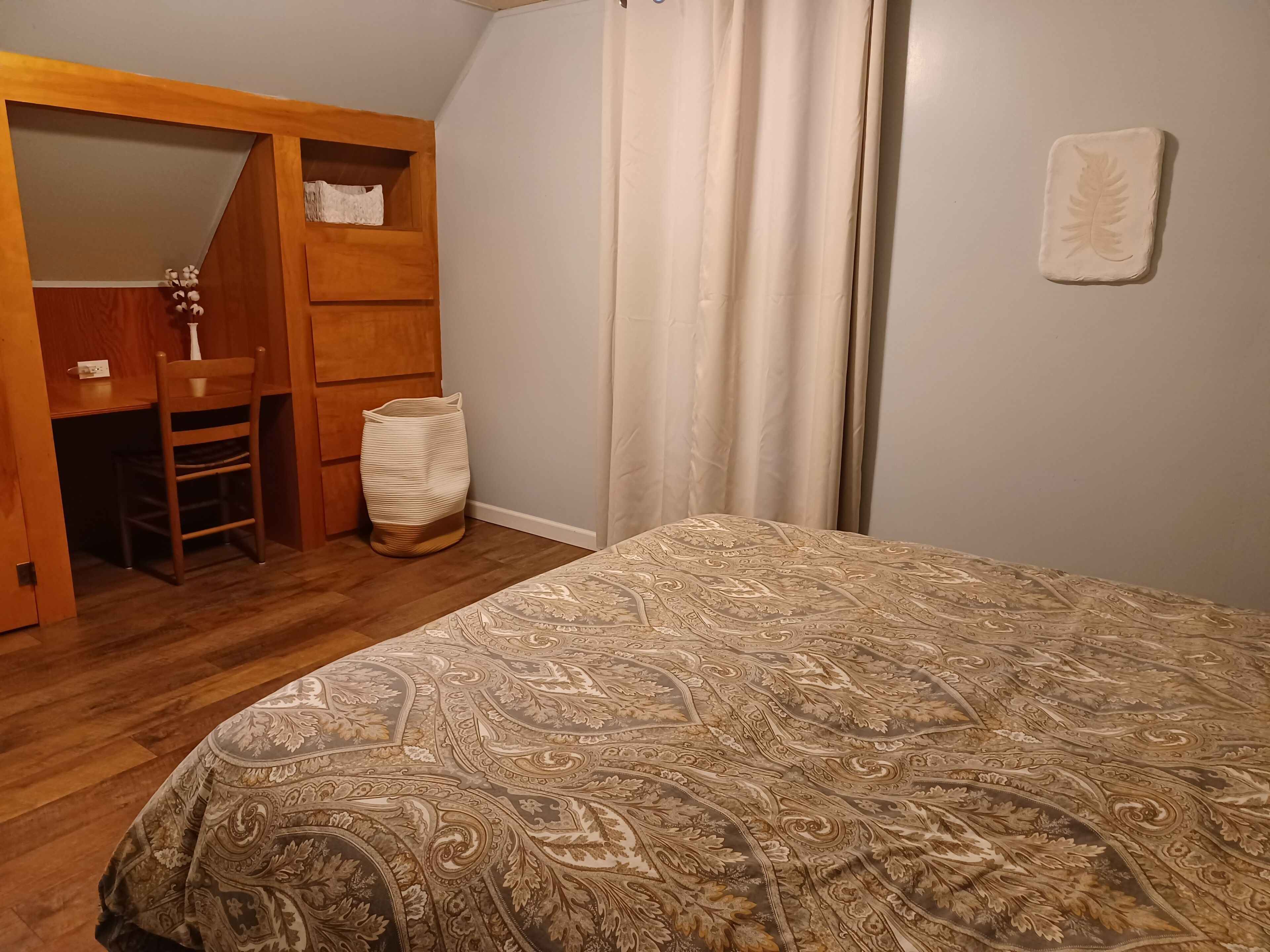 Une chambre à coucher avec une couvre-lit à motifs, une armoire en bois et un petit coin bureau.