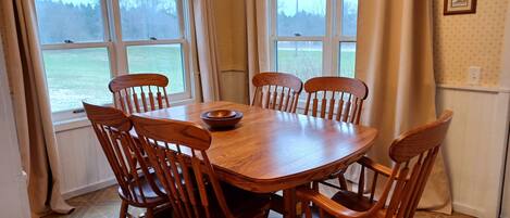 A dining room with a wooden table and chairs, large windows with curtains, and a view of a body of water.