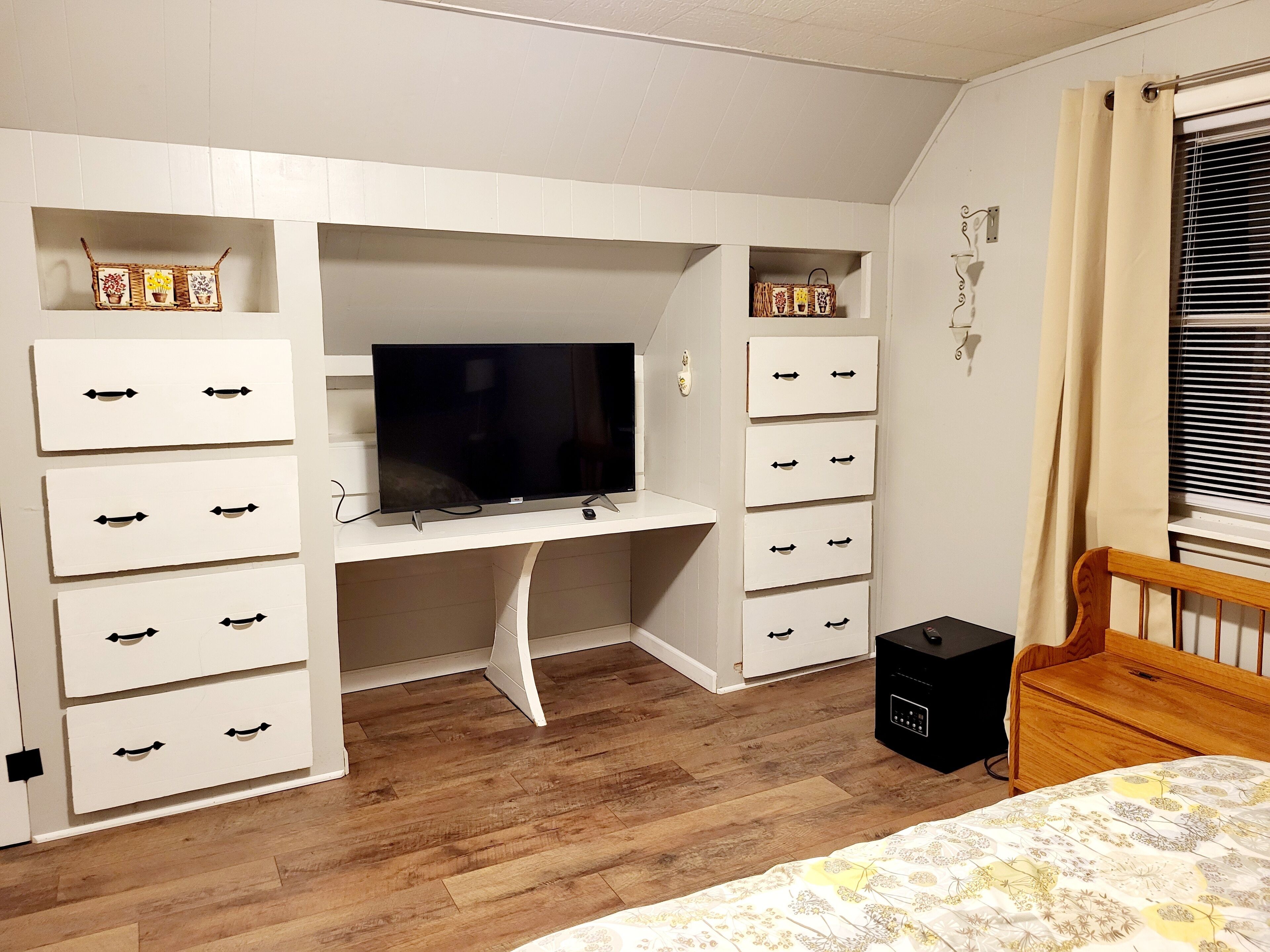 A bedroom with a built-in TV, white storage units, a wooden bed, and a bedside table.