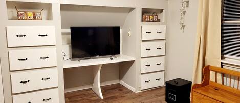 A bedroom with a built-in TV, white storage units, a wooden bed, and a bedside table.