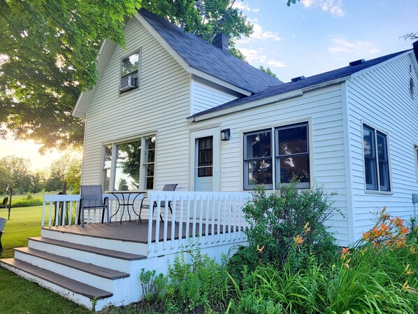 A white two-story house with a porch, a small deck, and a front yard with plants and flowers.