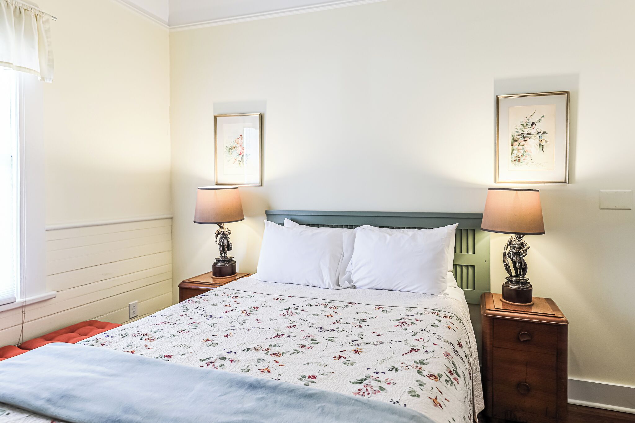 A neatly made bed with a floral bedspread, two bedside lamps, and two framed pictures on the wall.