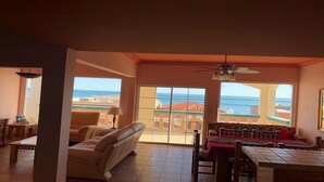 Un vaste salon doté d’une grande fenêtre offrant une vue sur la mer et les bâtiments.
