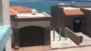 Une vue d’un bâtiment avec un toit recouvert de tuiles et une porte, une zone pavée et un ciel bleu dégagé.