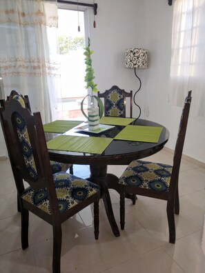 A dining table with a green placemat, surrounded by four chairs with patterned cushions. A decorative bottle with green leaves is placed on the table.
