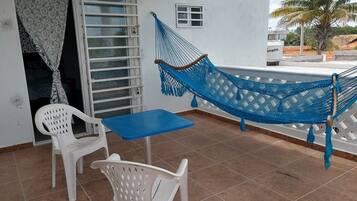 A balcony with a blue hammock, white plastic chairs, and a small table.